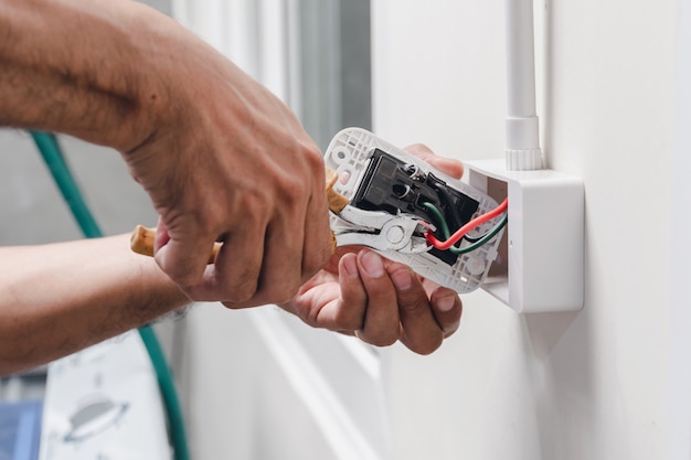 The technician is using a pliers wrench to install the power plug on the wall.