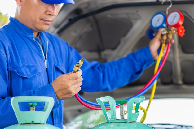 Tecnico che controlla il sistema di climatizzazione dell'auto ricarica del refrigerante riparatore che tiene lo strumento monitor per controllare e riparare il sistema di climatizzazione dell'auto riparazione dell'aria condizionata