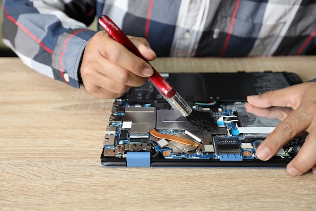 Technician man using a dusting brush to clean laptop computer