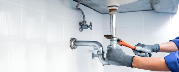 Technician plumber using a wrench to repair a water pipe under\
the sink concept of maintenance fix water plumbing leaks replace\
the kitchen sink drain cleaning clogged pipes is dirty or\
rusty