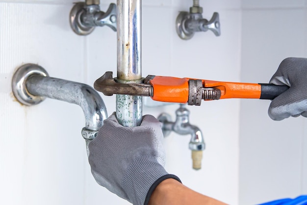 Technician plumber using a wrench to repair a water pipe under
the sink