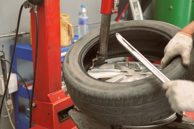 Photo technician removing rubber from car wheel disc & balancing tyre on balancer in auto repair garage