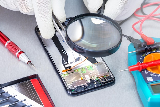 Technician repairing inside of mobile phone on desk. Process of mobile phone repair.