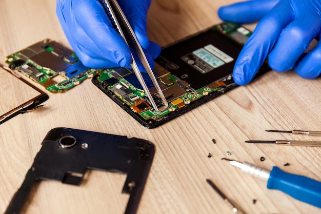 The technician repairing the smartphone's motherboard in the workshop on the table