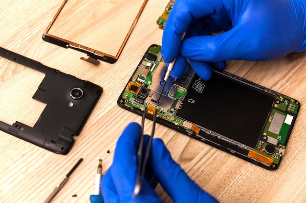 The technician repairing the smartphone's motherboard in the workshop on the table