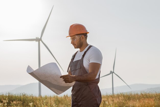 Technician standing of windmill farm with blueprints