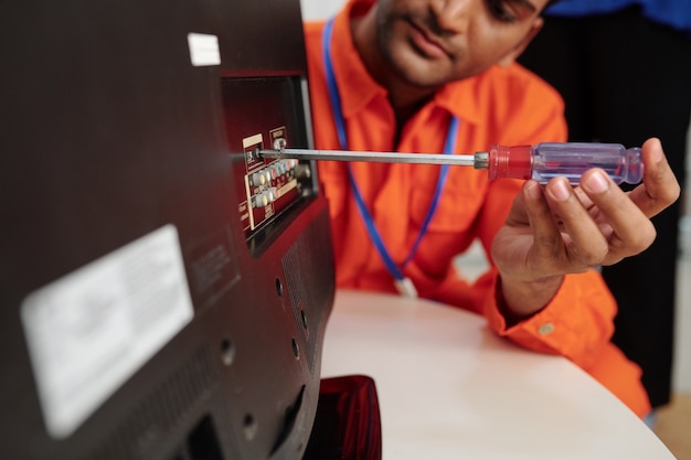 Technician using screwdriver when disassembling tv set to find breakage or install antenna