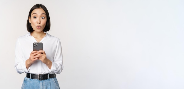 Technologie concept portret van aziatische vrouw met mobiele telefoon meisje smartphone houden en reageren verrast op mobiele telefoon melding app info witte achtergrond