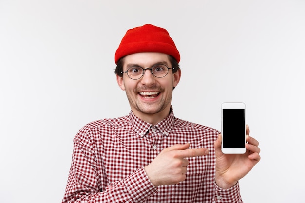Technologie en mensen concept. Close-up portret gelukkig lachend jonge bebaarde hipster man met mobiele telefoon, wijzend smartphone-display aanbevelen download app, opscheppen met geweldige match