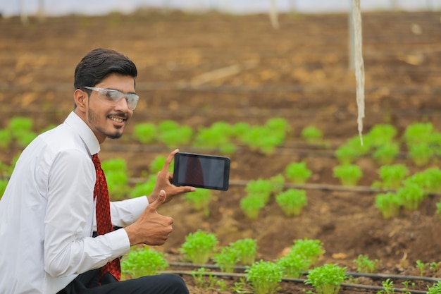 Technologie en mensen concept, jonge Indiase agronoom met behulp van tablet of smartphone op kas