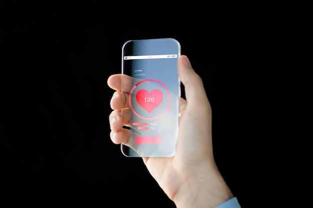 technologie, gezondheidszorg, toepassing en mensenconcept - close-up van mannenhand die transparante smartphone met rood hartpictogram op het scherm vasthoudt en toont en hartslag meet op zwarte achtergrond