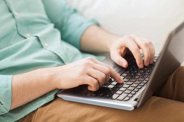 technologie, huis en lifestyle concept - close-up van de man die met een laptop werkt en thuis op de bank zit