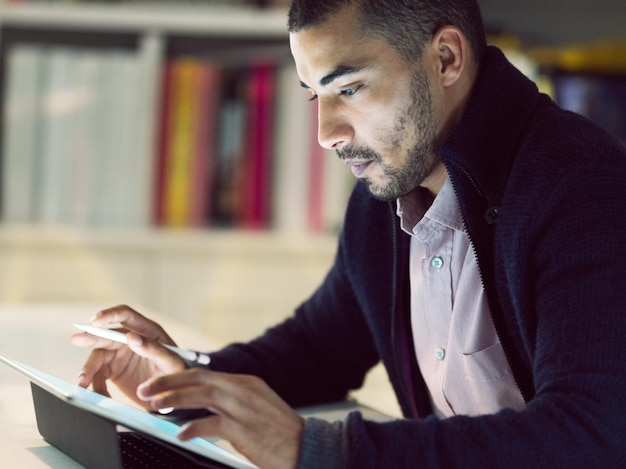 Technologie in de voorhoede van zijn carrière zetten Shot van een gefocuste jonge man die in de vroege avond op een digitale tablet in zijn thuiskantoor werkt