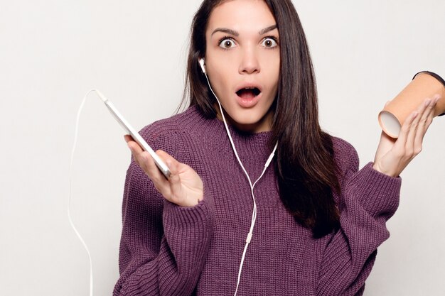 Technologie, levensstijl, internetverslaving en mensenconcept - jonge mooie vrouw met slimme telefoon. Gelukkig en lachende aantrekkelijke vrouw kijken naar de mobiele telefoon. Grijze muur op de achtergrond.