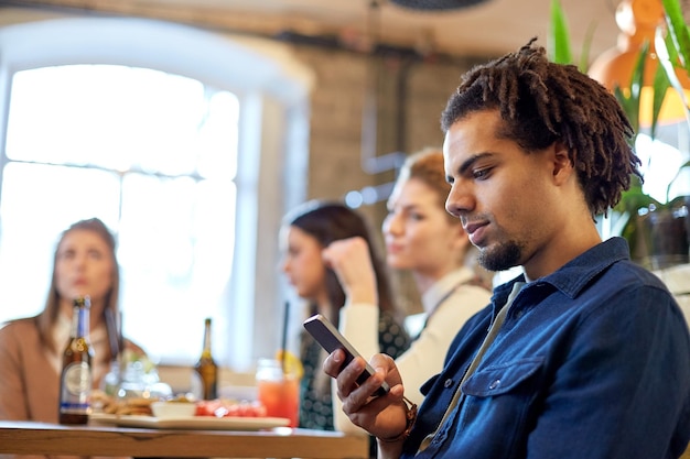 technologie, levensstijl, vakantie en mensenconcept - man met smartphone en vrienden in restaurant of bar