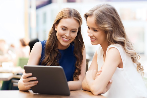 technologie, levensstijl, vriendschap en mensenconcept - gelukkige jonge vrouwen of tienermeisjes met tablet-pc in café buitenshuis