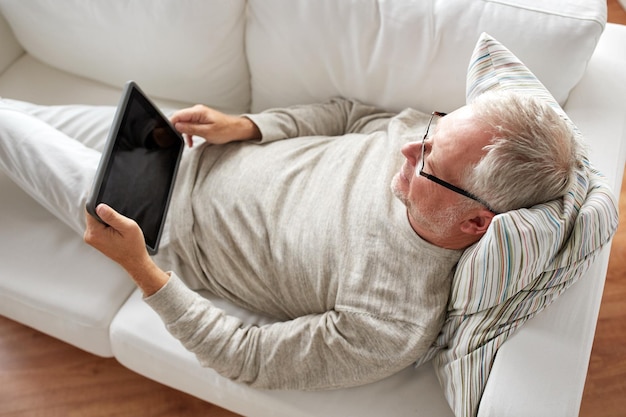 technologie, mensen en lifestyle concept - senior man met zwarte lege tablet pc computerscherm liggend op de bank thuis