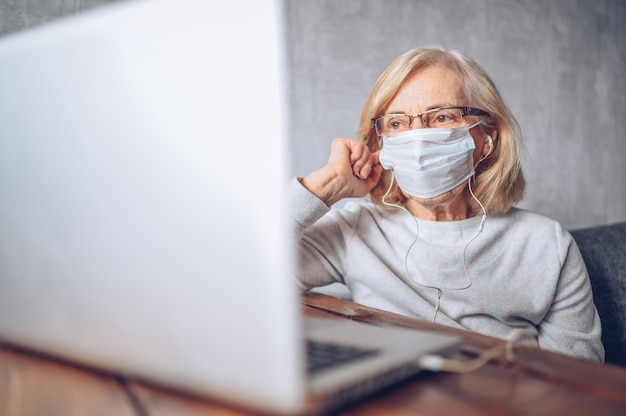 Foto technologie, ouderdom en mensenconcept - eenzame droevige oudere hogere vrouw in gezichts medisch masker die en een videogesprek met laptop thuis werken tijdens pandemie van het coronavirus covid19 werken. blijf thuis