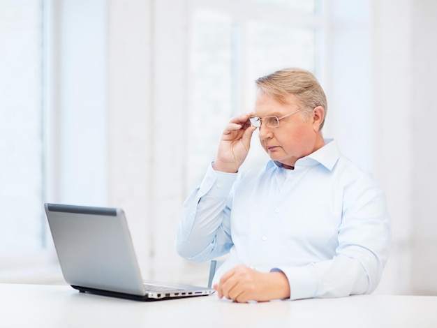 technologie, oudheid en lifestyle concept - oude man in brillen werken met laptopcomputer thuis