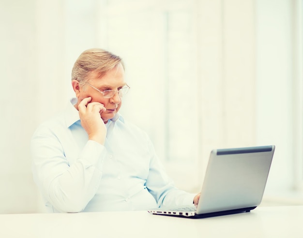 technologie, oudheid en lifestyle concept - oude man in brillen werken met laptopcomputer thuis