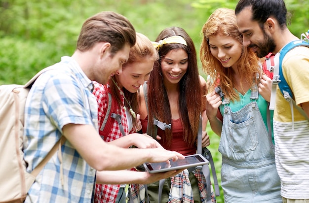 technologie, reizen, toerisme, wandelen en mensen concept - groep lachende vrienden wandelen met rugzakken en tablet pc-computer op zoek naar een locatie in het bos