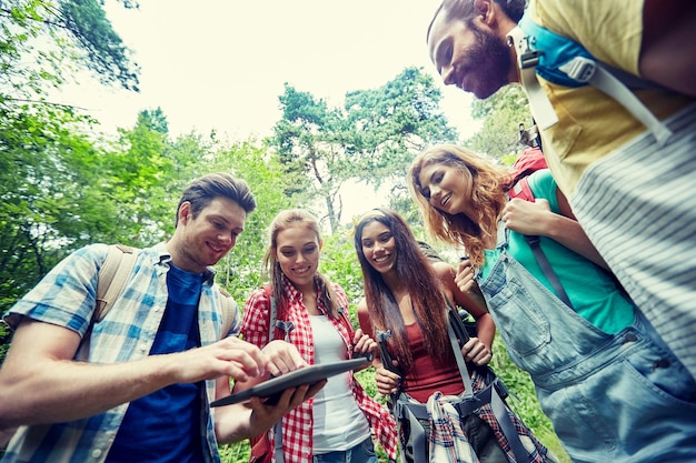 technologie, reizen, toerisme, wandelen en mensen concept - groep lachende vrienden wandelen met rugzakken en tablet pc-computer op zoek naar een locatie in het bos