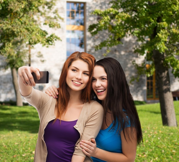 technologie, vriendschap en mensenconcept - twee glimlachende tieners die foto maken met smartphonecamera