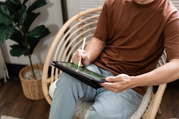 Technologieconcept De jonge man die op de stoel zit en zijn iPad vasthoudt en noteert