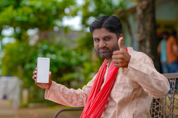 Technologieconcept: jonge Indiase boer die smartphone bij hem thuis laat zien