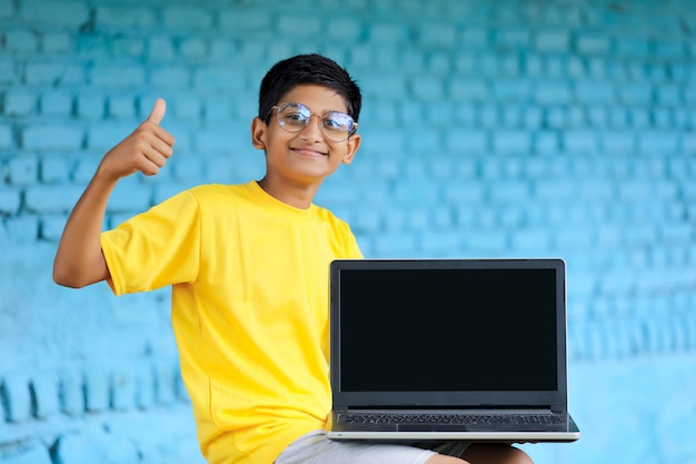 Technologieconcept: schattige Indiase kleine schooljongen die laptop gebruikt en klappen laat zien