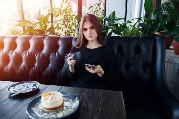 Technologieën, emoties, levensstijl, mensen, tieners concept - Jonge gelukkige vrouw leest op haar mobiele telefoon terwijl ze in een modern coffeeshopinterieur zit, prachtig hipstermeisje met mooie glimlach