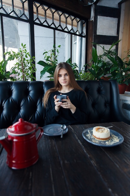 Фото Технологии, эмоции, образ жизни, люди, подростковая концепция - молодая счастливая женщина читает на своем мобильном телефоне, сидя в интерьере современного кафе, великолепная хипстерская девушка с красивой улыбкой