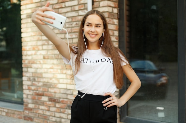Technologies,emotions, people, beauty, fashion and lifestyle concept - Carefree and happy, sunny spring mood. Charming young lady is making selfie on a camera. while on a walk in town outdoors