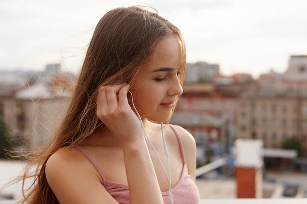 Foto tecnologie, emozioni, persone, musica, bellezza, moda e concetto di stile di vita - giovane donna con le cuffie che penzolano sul suo telefono cellulare mentre cammina in una strada urbana, vista dall'alto