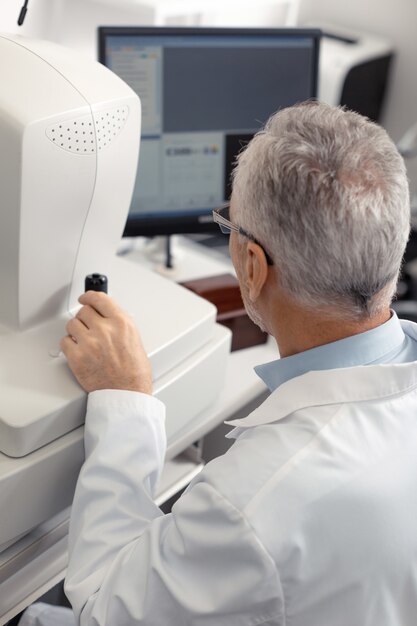 Technologies during examination. Grey-haired aged experienced ophthalmologist using technologies during examination