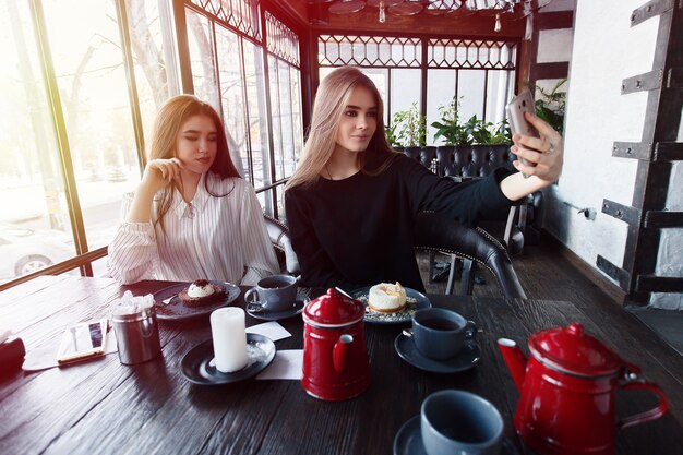 Technologies, lifestyle, food, people, teens and coffee concept - Two young women taking selfie with smart phone in the city center. Happiness concept about people and technology