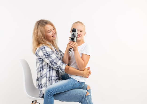 Photo technologies, photographing and family concept - mother and daughter using retro camera over white background.