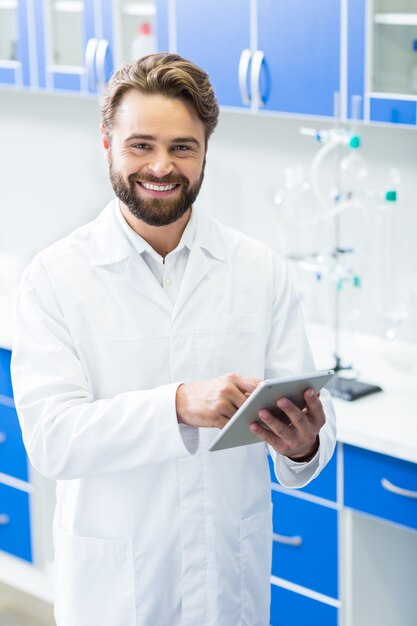 Technologische gadget. Opgetogen aardige knappe man die een tablet vasthoudt en glimlacht tijdens het werken in het biologische laboratorium