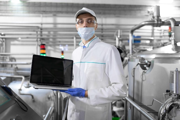 Technologist in a white coat with a laptop in his hands controls the production process in the dairy shop Place for writing Technologist with a laptop computer is at the factory