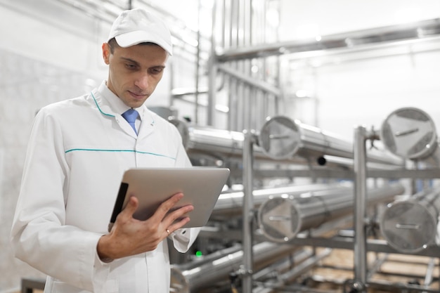 Technologist in a white coat with a tablet in his hands controls the production process in the dairy shop Quality control at the dairy plant