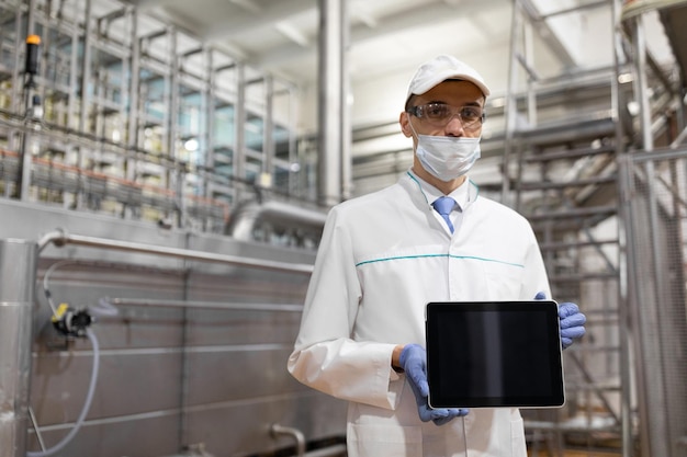 Technologist with grey tablet in his hands make a set up of the production line while standing at the department of dairy factory