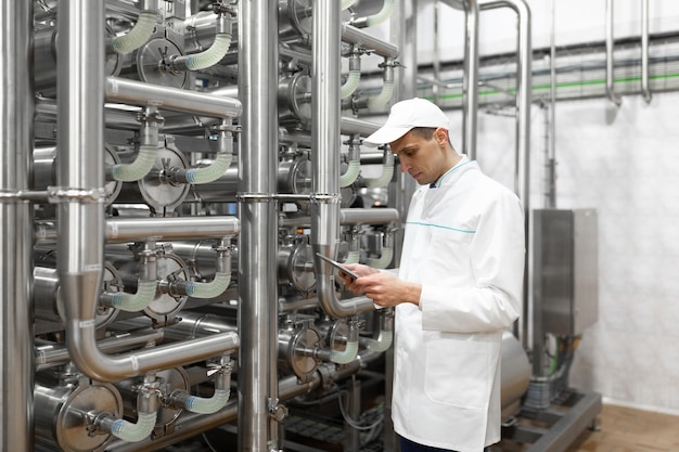 Technologist with grey tablet in his hands make a set up of the production line while standing at the department of dairy factory