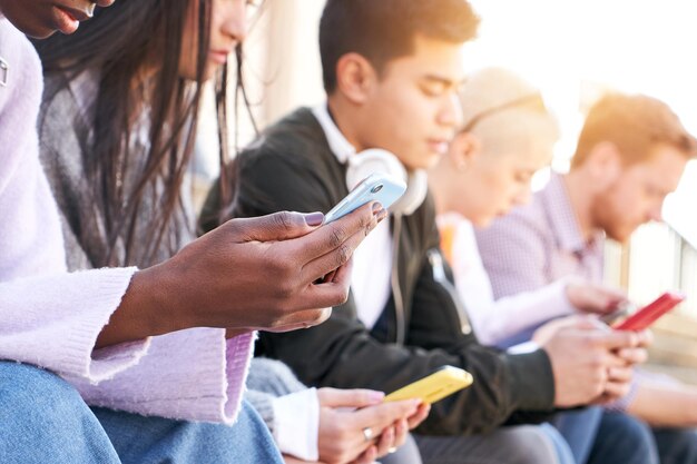 Gruppo di studenti multietnici dipendenti dalla tecnologia che usano i cellulari con un serio controllo facciale multimediale