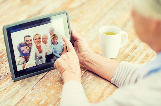 технология, возраст, воспоминания и концепция людей - счастливая пожилая женщина с планшетным компьютером просматривает семейный фотоальбом дома