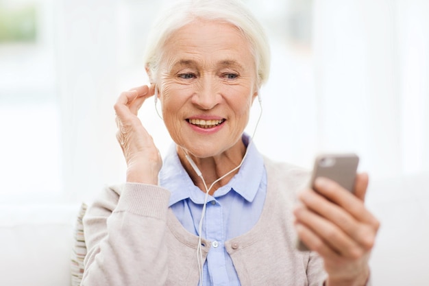 technology, age and people concept - happy senior woman with smartphone and earphones listening to music at home