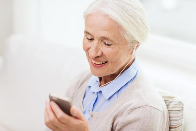 technology, age and people concept - happy senior woman with smartphone and earphones listening to music at home