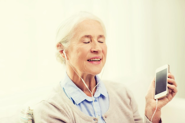 technology, age and people concept - happy senior woman with smartphone and earphones listening to music at home