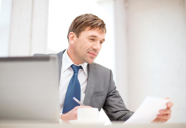 technology, business, internet and office concept - handsome businessman working with laptop computer, coffee and documents