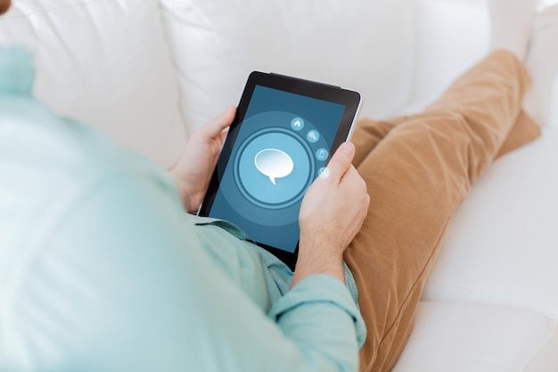 technology, business, leisure and people concept - close up of man holding tablet pc computer with text bubble icon on screen sitting on sofa at home