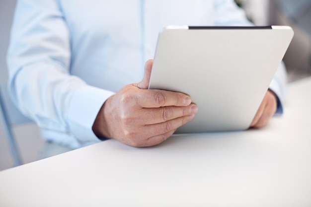 technology, business, retirement, people and leisure concept - close up of senior man hands with tablet pc computer at table in office